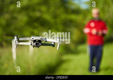 Nürtingen, Germany - May 29, 2021: The drone Dji air 2s. Grey unmanned aircraft system hovers over a green meadow. Pilot out of focus in background. F Stock Photo