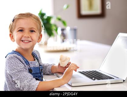 The next big thing in IT. Portrait of a happy little girl using a laptop while having a snack. Stock Photo