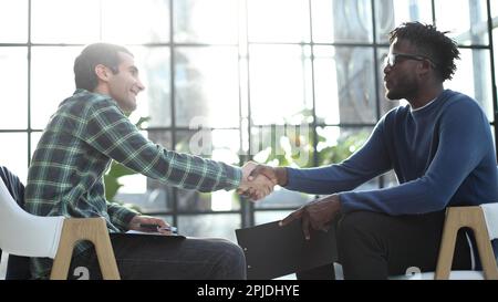 Business partners shaking hands sit on chairs in office lobby start or finish successful negotiations. Stock Photo