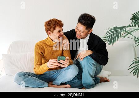 Happy gay couple sitting on the sofa using a mobile Stock Photo