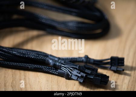 Tangled black computer cables lying on a brown wooden table Stock Photo