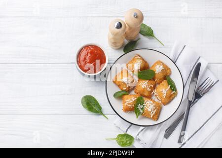 Deep fried traditional italian dish ravioli dumplings stuffed with spinach and cheese served with marinara tomato dipping sauce closeup on the wooden Stock Photo