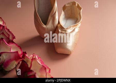 new ballet slippers lying on pink background with roses. elegant ballet shoes with bouquet Stock Photo