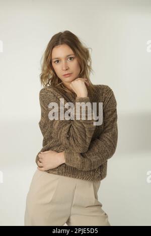 Fashion portrait of young woman in brown winter sweater and beige wide pants on the white background Stock Photo