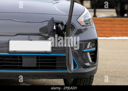 Electric car plugged in to recharge battery, detail, front view. No people, logos etc removed. Stock Photo