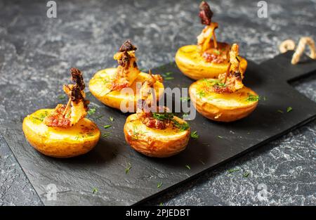Golden potato halves baked with bacon served on a black board. Dark background, selective focus, close up. Stock Photo