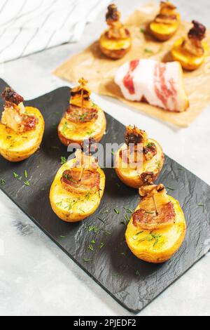 Golden potato halves baked with bacon served on a black board. Top view ...