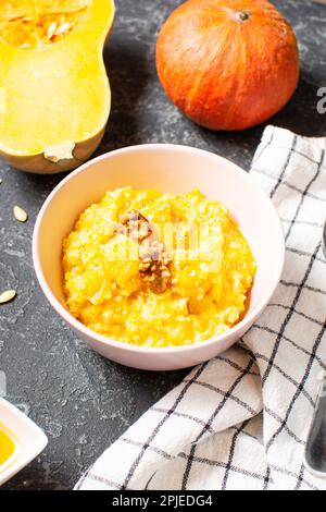 Rice milk pumpkin porridge with walnuts, butter and honey on a black stone table. Healthy food. Stock Photo