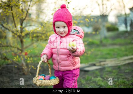 child collects colorful Easter eggs in basket. Easter egg hunt concept. Stock Photo
