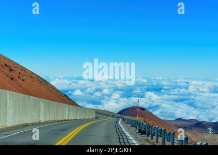 Winding road leading among volcanic hills of Mauna Kea high above the clouds. Stock Photo