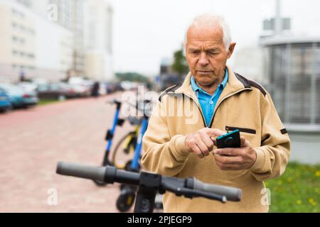 Old man using smartphone to activate e-scooter Stock Photo