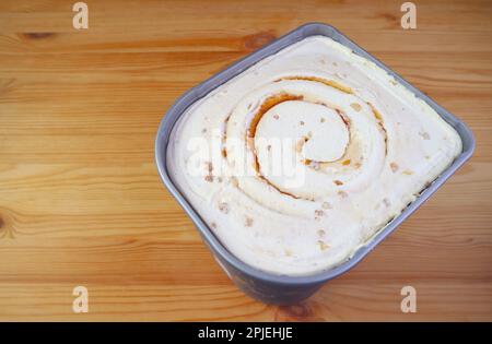 Tub of Delectable Salted Caramel Macadamia Nut Ice Cream Isolated on Wooden Table Stock Photo