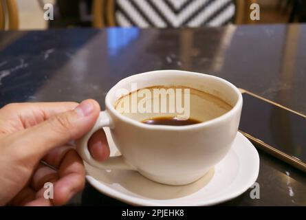 Hand Holding a Half Cup of Hot Coffee beside with Cellphone on Black Table Stock Photo