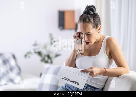 Surprised woman is on a phone with call center surprised from receiving a printed reminder by mail. Stock Photo