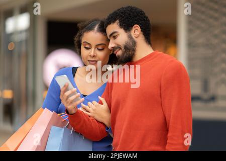 Diverse Couple Shopping Online Using Smartphone Together At Mall Outdoor Stock Photo