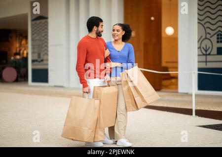 Multiethnic Couple Shopping Standing With Many Paper Shopper Bags Outdoors Stock Photo