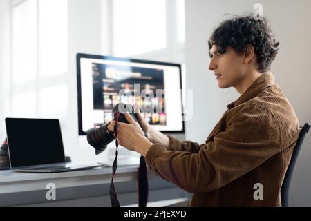 Positive male photographer holding camera while working with photos, looking through taken pictures, working at studio Stock Photo