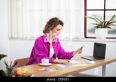 Female Graphic Designer Working With Laptop And Color Swatches In Home Office Stock Photo