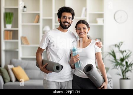 Young indian couple holding yoga mats at home and smiling at camera Stock Photo
