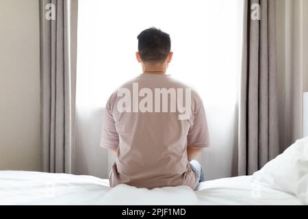 Unhappy man sitting alone on bed alone at home Stock Photo