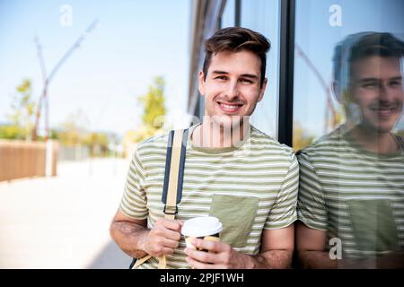 Happy young student smiling with backpack drinking a take away coffee at the campus. Stock Photo