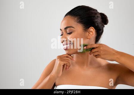 Pretty young black woman massaging face with gua sha Stock Photo