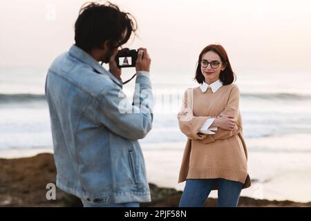 Happy young indian guy photographer in casual make photo on camera of european woman in glasses Stock Photo