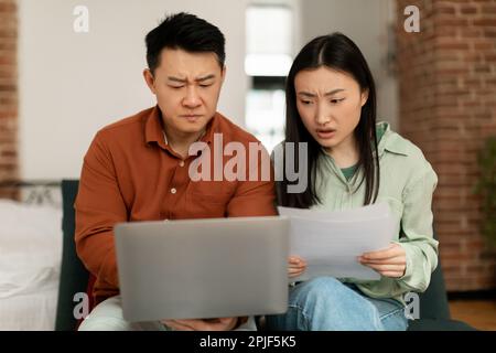Concerned asian spouses sitting with laptop, checking bills, making countings, working on family budget Stock Photo