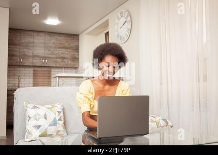 African American woman freelancer, work from home. woman in front of laptop is happy, smiling. Winning lottery, hired, stocks have risen, cryptocurren Stock Photo