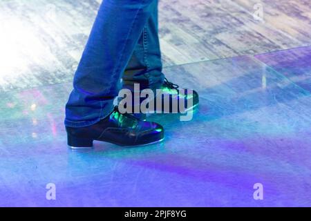 Men's legs in motion in stage trousers with stripes and leather shoes for Irish dancing on the floor. Black work boots for tap dancing with reflection Stock Photo