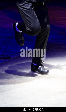 Men's legs in motion in stage trousers with stripes and leather shoes for Irish dancing on the floor. Black work boots for tap dancing with reflection Stock Photo