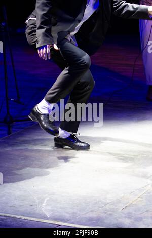 Men's legs in motion in stage trousers with stripes and leather shoes for Irish dancing on the floor. Black work boots for tap dancing with reflection Stock Photo