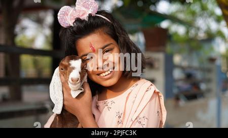 A baby goat being held by a shy little Indian girl aged 10 years old peeping out from behind it. Stock Photo
