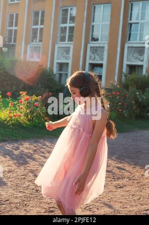 Beautiful little girl listen to music in sunny spring park. Happy cute kid having fun outdoors at sunset. Soft focused Stock Photo