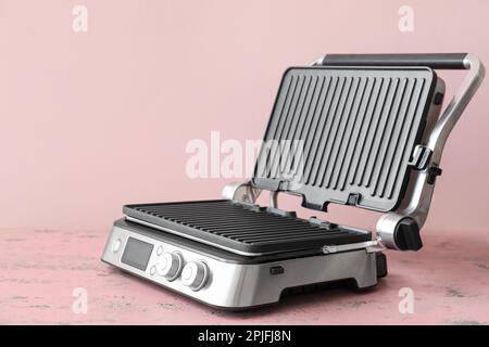 Modern electric grill with open lid on pink table Stock Photo