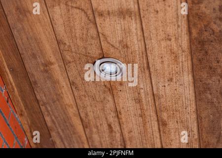 A portrait of a weather sealed light spot put in the wooden planks of a roof overhang. The lamp is turned off. Stock Photo