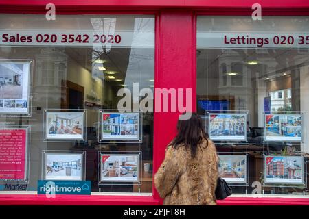 London- February 2023: Young woman looking at house adverts in estate agent window in Hammersmith, West London Stock Photo