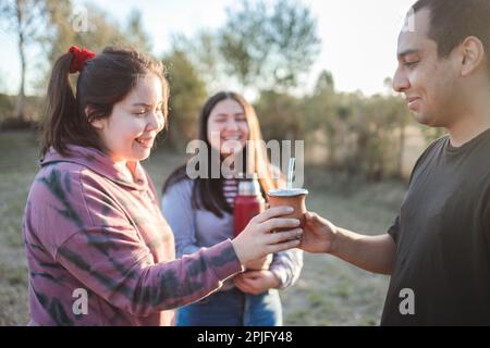 https://l450v.alamy.com/450v/2pjfy48/group-of-smiling-friends-drinking-yerba-mate-using-a-thermos-with-hot-water-in-the-countryside-at-sunset-2pjfy48.jpg