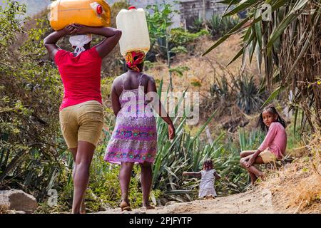 Two women and a child carrying water canisters as heavy load on their heads, Santiago Island, Cape Verde Islands Stock Photo