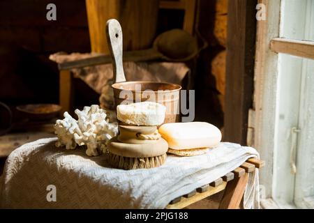 Traditional Finnish wooden sauna in details. Set of bath accessories - loofah organic sponge, natural brush and handmade soap.  Old rustic interior. Stock Photo