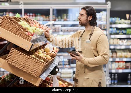 Waist up portrait of male worker in supermarket checking fresh produce in fruit and vegetables aisle Stock Photo