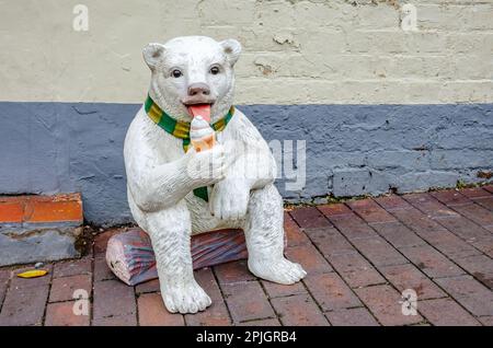 A model of a white bear sat on a log eating an ice cream on the pavement at Ironbridge in Shropshire, UK outside an ice cream shop Stock Photo