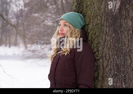 sad woman leaning against tree in snow suffering from winter depression Stock Photo