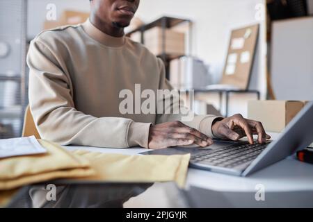 Close-up of young male manager of storage room typing on laptop keyboard while sitting by workplace and checking new online orders Stock Photo