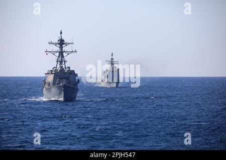 ATLANTIC OCEAN (March 30, 2023) Arleigh Burke-Class guided missile destroyer USS Thomas Hudner (DDG 116), left and Ticonderoga-class guided missile cruiser USS Normandy (CG 60) sail in formation during an integrated live-fire event, March 30, 2023. McFaul, as part of the Ford Carrier Strike Group, is underway in the Atlantic Ocean completing its Composite Training Units Exercise (COMPTUEX), an intense, multi-week exercise designed to fully integrate a carrier strike group as a cohesive, multi-mission fighting force and to test their ability to carry out sustained combat operations from the sea Stock Photo