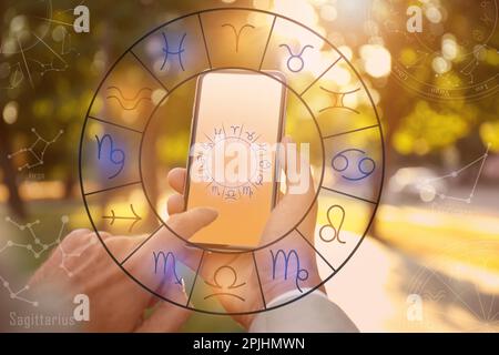 Man with smartphone reading daily horoscope outdoors, closeup Stock Photo