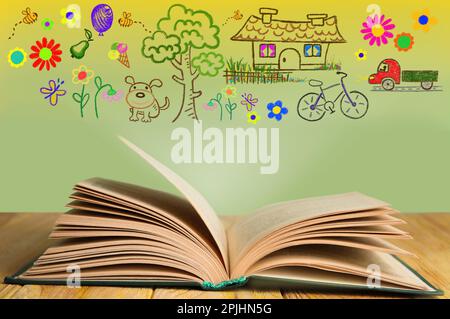 Open book on wooden table against wall with drawings Stock Photo
