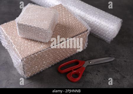 Cardboard boxes, bubble wrap and scissors on dark grey table Stock Photo