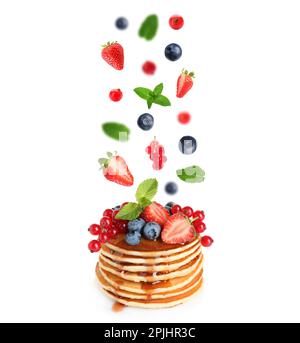 Fresh berries and mint leaves falling onto stacked pancakes against white background Stock Photo