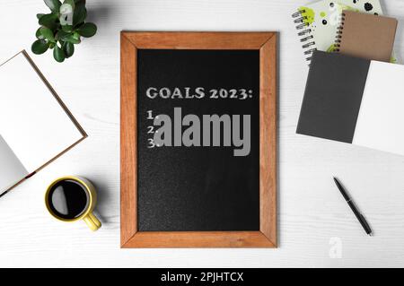 Blackboard with phrase GOALS 2023 and empty checklist on white wooden background, flat lay Stock Photo